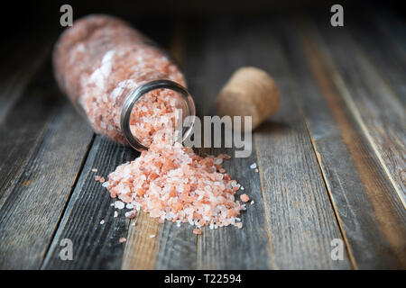 Rosa Himalaya Salzkristalle in der Glasflasche und kleine Schüssel auf Holztisch. Stockfoto