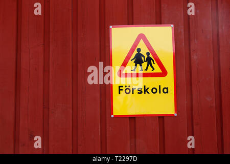 Gelbes Schild mit dem Hüten von Kindern Verkehrszeichen und Text auf Schwedisch für Kindergarten auf einem roten Holzwand. Stockfoto