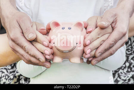 Das Kind und die Eltern sind mit einem Sparschwein in der Hand. Natur. Stockfoto