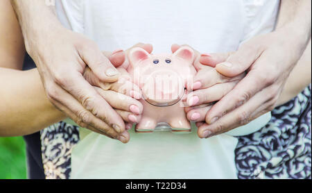 Das Kind und die Eltern sind mit einem Sparschwein in der Hand. Natur. Stockfoto