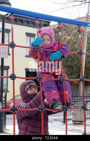 Eine Mutter mit ihrer kleinen Tochter (4 Jahre alt) auf einem Klettergerüst in Quebec im Winter Stockfoto