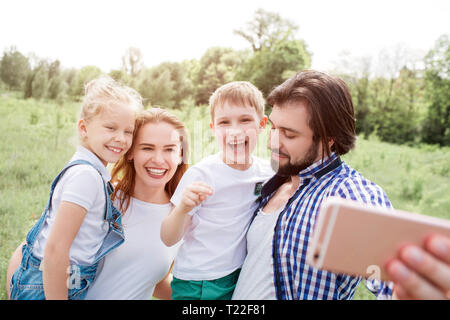 Wunderschöne Familie nimmt selfie. Kerl hält Telefon und blickte nach unten. Alle anderen sind auf der Suche nach Telefon- und lächelnd Stockfoto