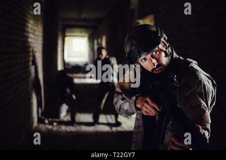 Drei Soldaten stehen in dunklen Flur und wartet. Der Kerl vor ist auf der Suche nach rechts und Halten der Waffe in der Hand. Die anderen zwei sind s Stockfoto