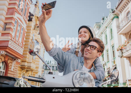 Kerl sitzt auf Motorrad mit seiner Freundin und unter selfie. Er hält das Telefon in der Hand. Sie lächeln und Posieren vor der Kamera Stockfoto