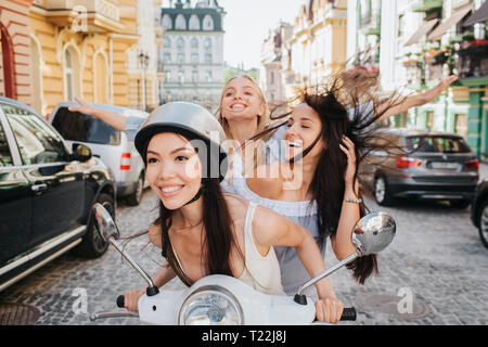 Drei Mädchen sind Reiten auf einem Motorrad. Chinesische Mädchen ist, die sich in einem von vorn. Brunette Mädchen sitzt in der Mitte. Der letzte ist blondes Mädchen. Sie sind sm Stockfoto