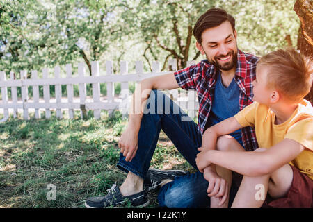 Bärtiger Mann sitzt im Schatten und bei kleinen Jungen. Kind ist auf der Suche nach seinem Vater. Sie ist entspannend und zusammen Chillen Stockfoto