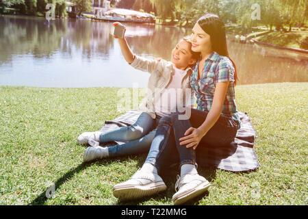 Ein weiteres Bild von kleine Familie zusammen zu sitzen und auf Kamera posieren. Kleines Mädchen hält Telefon und unter selfie. Sie Lächeln Stockfoto