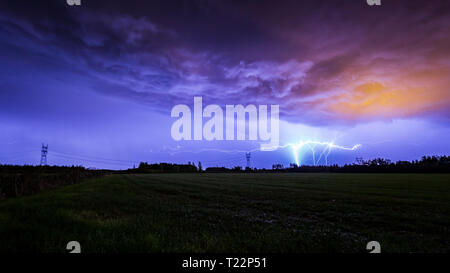 Boden GC Blitz gegen eine dramatische Sturm Himmel über ein Feld während der Nacht zu Cloud. Leichte Verschmutzung verursacht eine Orange glühen in der cloudscap Stockfoto