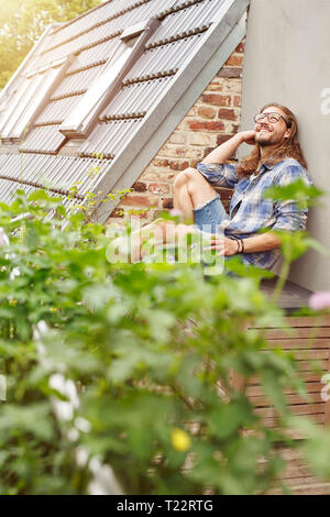 Glückliche junge Mann sitzt auf seinem Balkon, entspannend Stockfoto