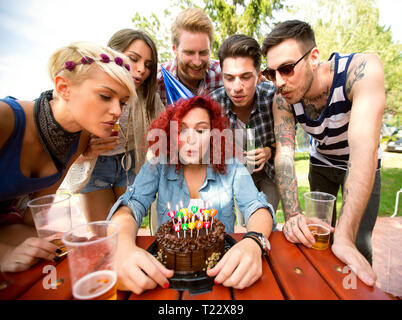 Curly Ingwer erfreut Geburtstag Mädchen blasen bunte Kerzen auf der Geburtstagstorte in der Natur Stockfoto