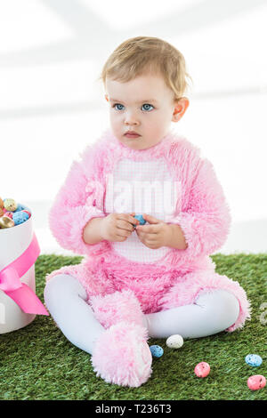 Adorable Kind in rosa Flauschige kostüm Holding blau Wachtelei beim Sitzen in der Nähe der Box mit Ostereiern isoliert auf weißem Stockfoto