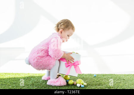 Adorable kid in rosa Flauschige kostüm Holding Box mit rosa Schleife und bunte Ostereier isoliert auf weißem Stockfoto