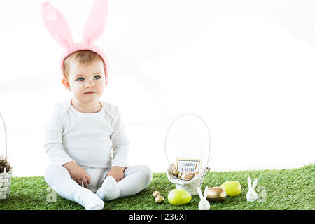 Cute Baby Sitting in der Nähe von Stroh Korb, Ostereier und dekorative Kaninchen isoliert auf weißem Stockfoto