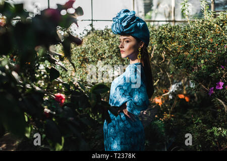 Wunderschöne junge Frau im blauen Kleid und Turban in Orangerie Stockfoto