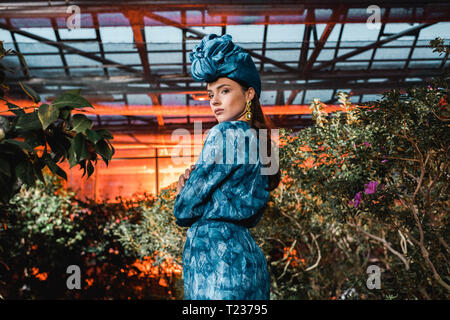 Wunderschöne junge Frau im blauen Kleid in Turban in Orangerie Stockfoto