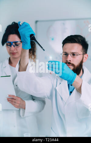 Jungen männlichen Forschern mit Tropfer und Reagenzglas, das Tragen von weißen Mantel. Stockfoto