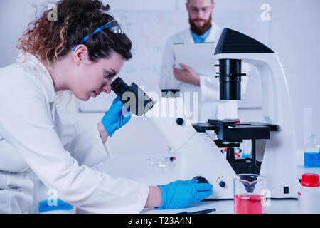 Junge weibliche Wissenschaftler tun Test im Labor, in der männliche Wissenschaftler hinter. Stockfoto