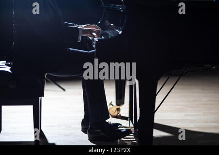 Ein eleganter Mann in einem schwarzen Anzug spielen Grand Piano auf der Bühne in einem Konzertsaal, aus der Nähe. Stockfoto