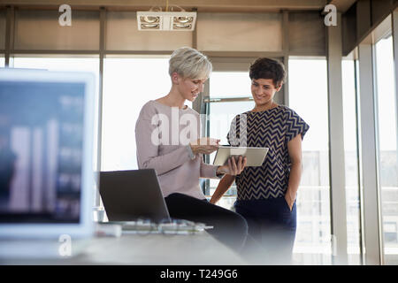 Zwei lächelnde Geschäftsfrauen sharing Tablette im Büro Stockfoto