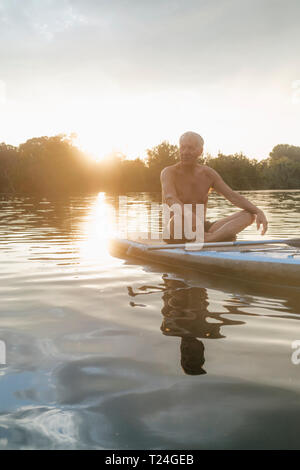 Älterer Mann sitzt auf SUP Board bei Sonnenuntergang Stockfoto