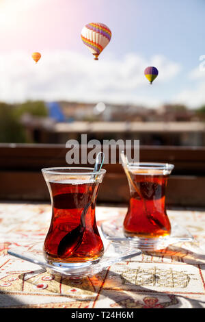 Türkischer Tee im Restaurant und Heißluftballon fliegen über blauen Himmel in Kappadokien, Türkei Stockfoto