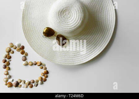 Sommer mode Deko von Herzförmige seashells konzipiert, sun Strohhut und Pilotenbrillen. Ferienhäuser Hintergrund. Stockfoto