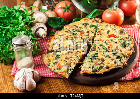 Frittata aus Eiern, Pilzen und Spinat auf einem Schneidebrett. Italienische Küche Stockfoto