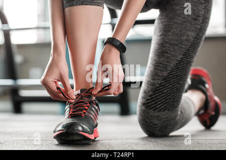 Junge Frau im Gym gesunde Lebensweise stehen auf Knie binden Schnürsenkel Sneakers auf einem Fuß close-up Stockfoto