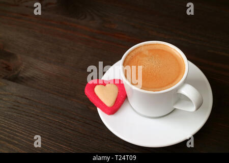 Heiße Tasse Kaffee mit einem Herzförmigen Cookie auf dunkelbraunen hölzernen Tisch Stockfoto