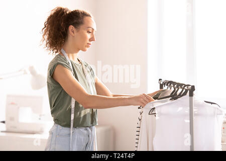 Junge brünette Frau in Freizeitmode suchen durch Kleidung, während eine Wahl getroffen haben, als ein Beispiel für neue Fashion Kollektion Stockfoto