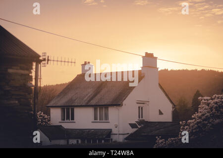 Ein Gemütliches Reetdachhaus Englisch Cottage mit dem warmen orange Sonne hinter ihn in der Mitte der Feder Stockfoto