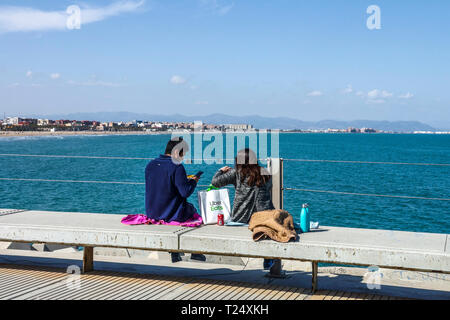 Das Paar machte ein Picknick auf dem Betonpier mit Blick auf das Meer und Malvarrosa Strand das Essen wurde von Uber Eats, Valencia Hafen, Spanien Meerblick geliefert Stockfoto