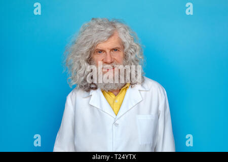 Alte langhaarigen Mann, der Doctor's Kleid studio isoliert auf blauen Wand suchen Kamera lächelt Fröhlich Stockfoto