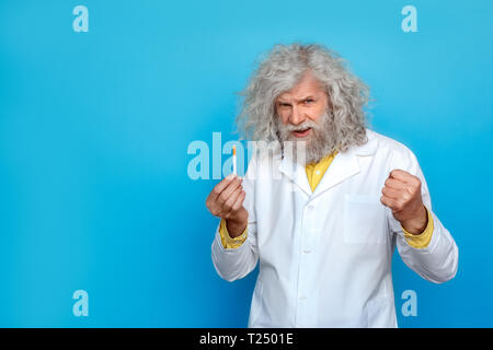 Alte langhaarigen Mann, der Doctor's Kleid Studio auf der blauen Wand holding Zigarette und Hand in Faust suchen Kamera isoliert Sprechen unglücklich Stockfoto