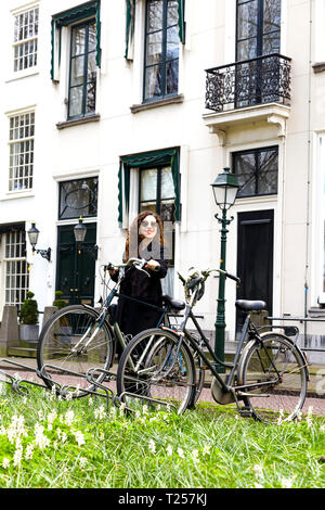 Ein junges Mädchen steht auf einem weißen Haus Hintergrund mit einem Fahrrad. Frau in Sonnenbrille parken ihre vintage Bike auf der Straße in der Altstadt. Stockfoto