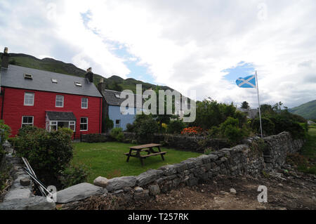 Dorf Dornie, Schottland - 12 Juni 2014: Einige farbige Häuser mit Gärten und die schottische Flagge im Hintergrund, in der Nähe von Eilean Donan Castle Stockfoto