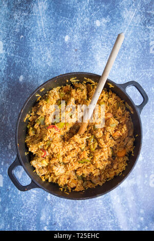 Blick von oben auf die gekochten Afrikanischen jollof Reis Rezept in einer tiefen Pfanne und einem Löffel aus Holz innen. Grauer Hintergrund. Stockfoto
