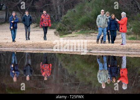 Die Leute, die einen Spaziergang entlang der Küste genießen, spiegeln sich im ruhigen Wasser von Loch Morlich in der Nähe von Aviemore in den schottischen Highlands wider Stockfoto