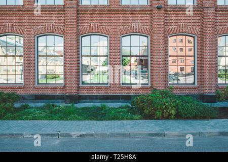 Bürogebäude im Loft-Stil. Große Fenster. Red brick wall. Grüne Büsche auf der Mitte. Flache Fassade Zusammensetzung Stockfoto