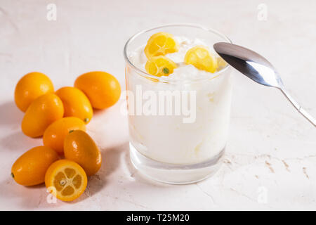 Joghurt mit Scheiben von kumquat in Glas mit Metall Löffel und ganze Früchte auf weißem Hintergrund. Stockfoto