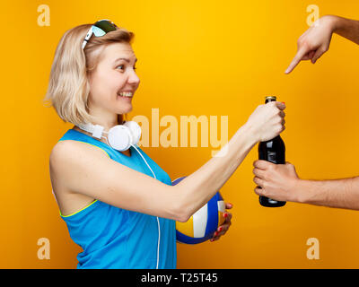 Frau entscheidet zwischen Volleyball und Flasche Bier im Studio Stockfoto