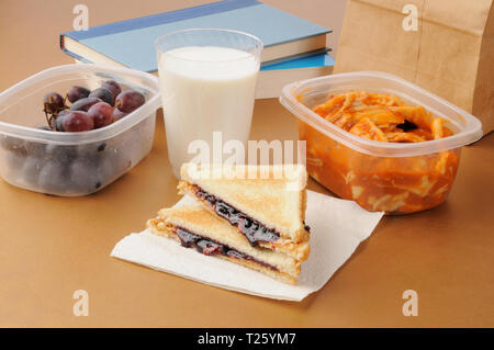 Eine Schule Lunchpaket mit Büchern, Trauben, Ravioli, und ein Sandwich mit Erdnussbutter und Marmelade Stockfoto