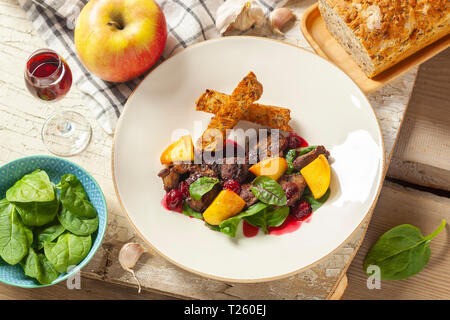 Flambierte Hühnerleber in Kirsch, Spinatblätter, karamellisierten Äpfel mit Knoblauch und Rosmarin, Kirschen, Toast Stockfoto