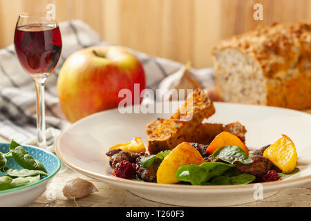 Flambierte Hühnerleber in Kirsch, Spinatblätter, karamellisierten Äpfel mit Knoblauch und Rosmarin, Kirschen, Toast Stockfoto