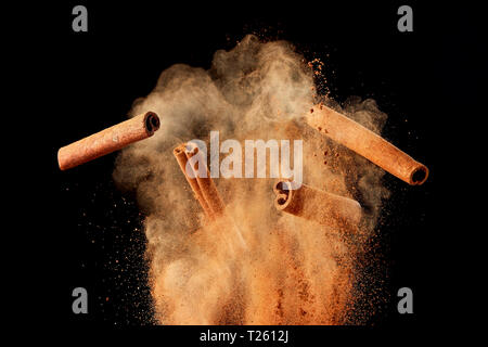 Essen Explosion mit Zimtstangen und Pulver auf schwarzem Hintergrund. Stockfoto