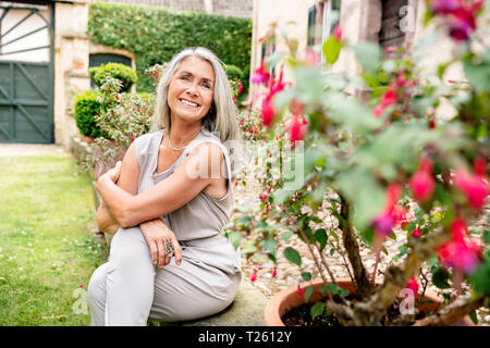 Gerne Frau mit langen grauen Haaren im Garten sitzen Stockfoto
