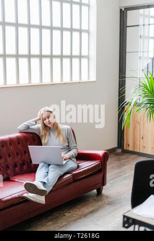 Lächelnde junge Frau sitzt auf der Couch mit laptop Stockfoto