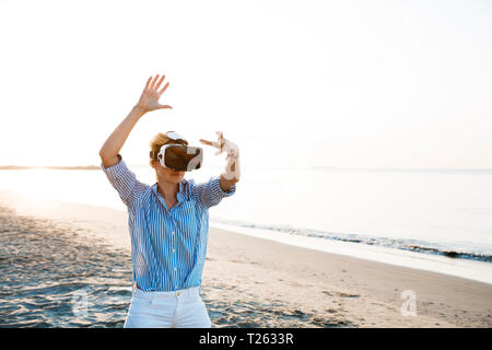 Blonde Frau tun Art von Yoga Übungen auf einem Strand in Thailand mit 3D Virtual Reality goggles Stockfoto