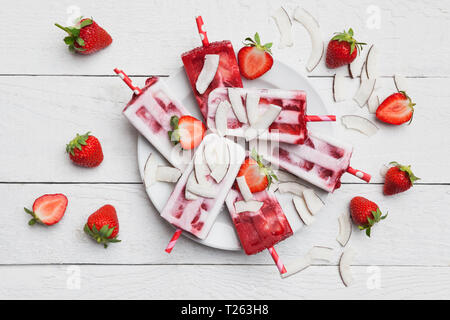 Selbstgemachte Erdbeer Kokos Eis am Stiel mit frischen Erdbeeren und Kokosnuss Scheiben auf Platte Stockfoto