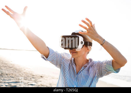 Blonde Frau tun Art von Yoga Übungen auf einem Strand in Thailand mit 3D Virtual Reality goggles Stockfoto